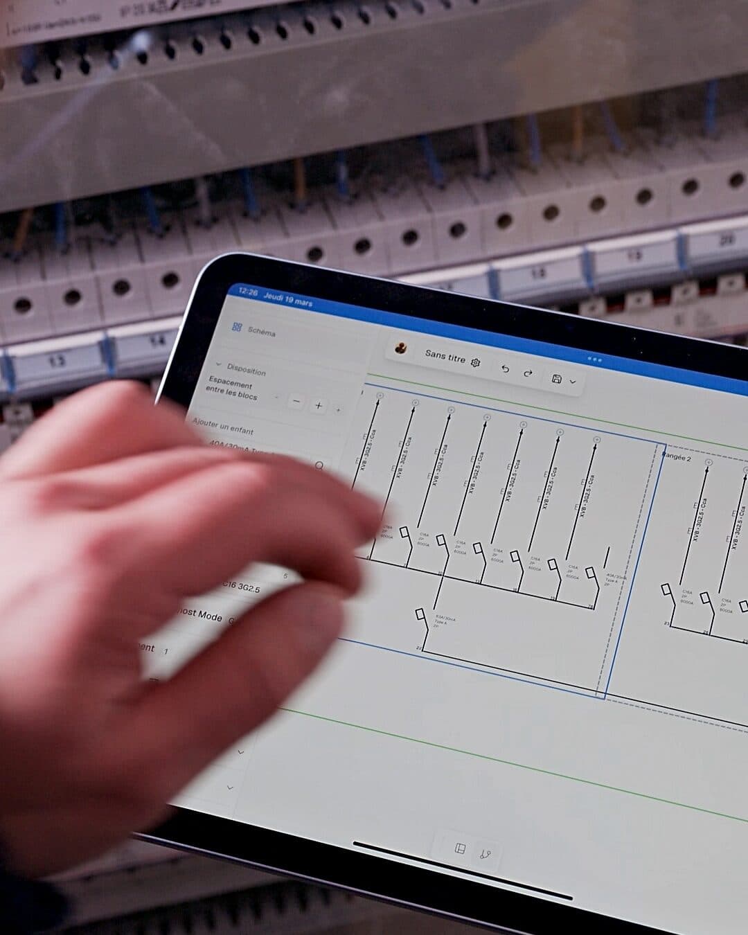 Tablette en main devant un tableau électrique, schéma unifilaire ElectriCAD à l'écran