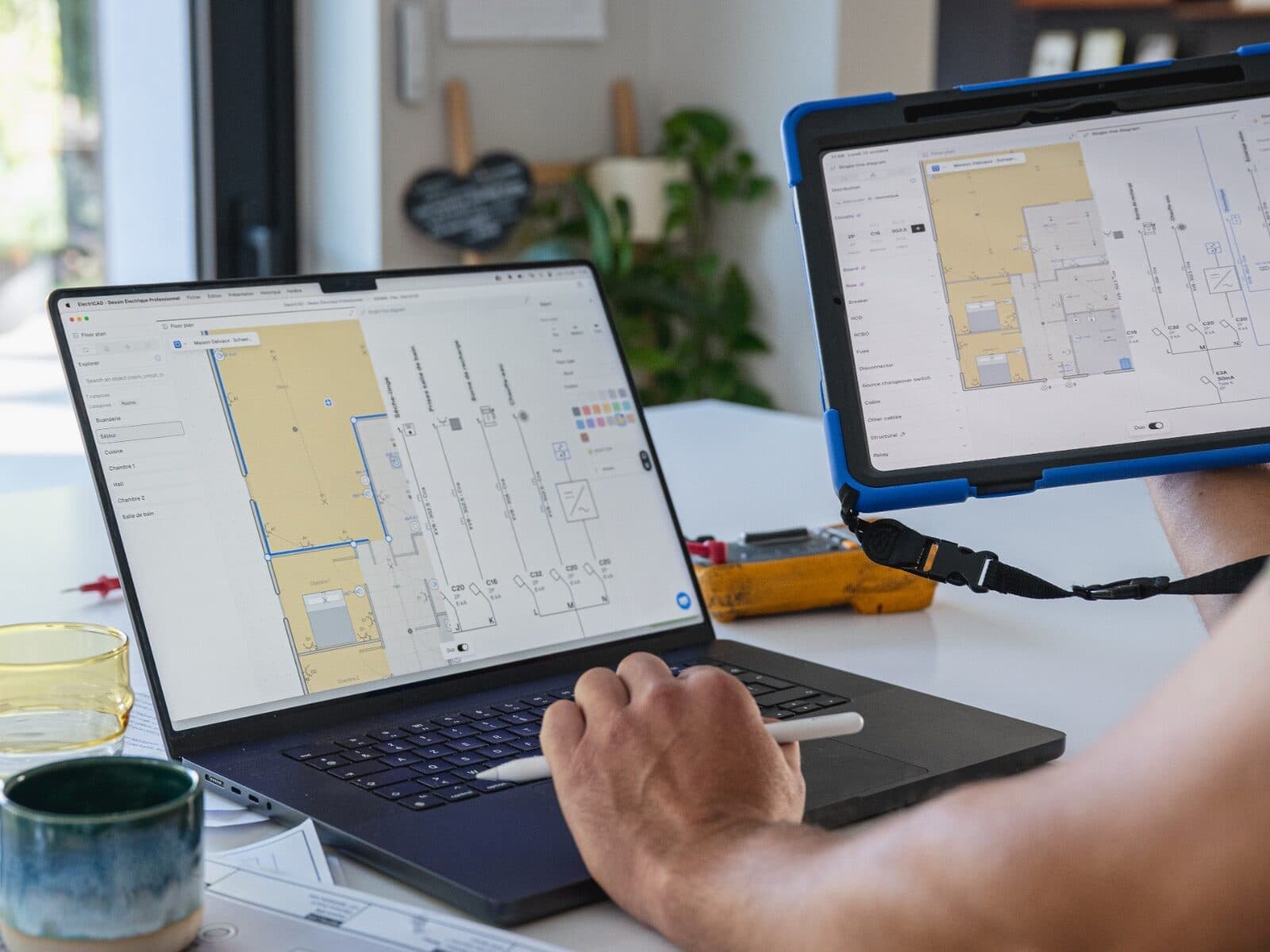 Photo : le même projet de démo ouvert sur un ordinateur portable et sur une tablette tenue à côté, le plan et le schéma unifilaire côte à côte